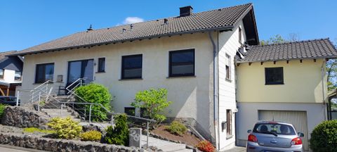Ein modernes Wohnhaus mit einem ansprechenden Garten. Der Himmel ist blau und es ist sonnig.
