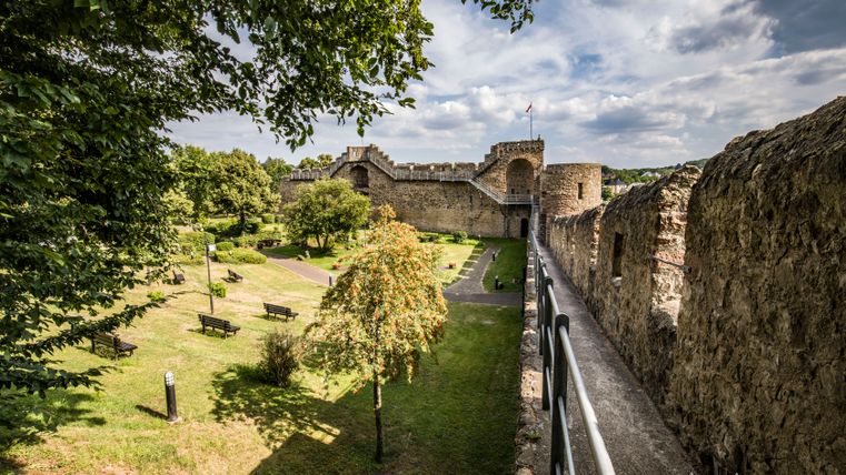 View of a historic city wall with garden and trees in the foreground.