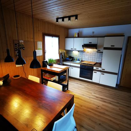 Eine moderne Küche mit Holzdecken und hellen Möbeln. Der Essbereich ist schlicht eingerichtet mit einem großen Tisch und Stühlen.