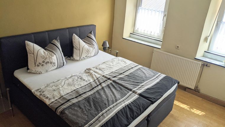 Ein gemütliches Schlafzimmer mit einem Doppelbett und dekorativen Kissen. Ein angenehmer Holzfußboden und Fenster sorgen für viel Tageslicht.