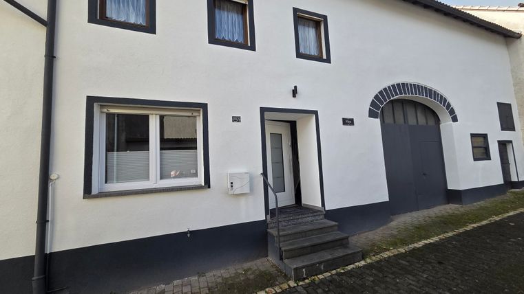Ein modernes Wohnhaus mit einer hellen Fassade und großen Fenstern. Die Treppe führt zum Eingang, daneben befindet sich eine große Toreinfahrt.