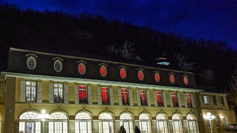 Ein historisches Gebäude bei Nacht mit roten Fenstern und einem dunklen Hintergrund. Die Szene wird von warmem Licht der Straßenlaternen erhellt.