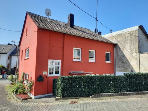 Ein rotes Haus mit einem gepflanzten Vorgarten. Es hat helle Fenster und eine klare blaue Himmel im Hintergrund.