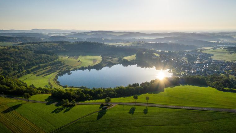 A vast landscape with a clear lake and green fields. The sun is shining, creating a peaceful atmosphere.