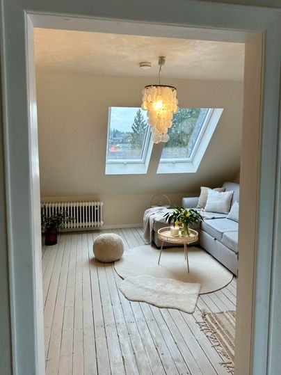Ein heller Wohnraum mit großen Fenstern und einem weißen Sofa. Der Raum ist modern und gemütlich eingerichtet mit einem Teppich und einer Pflanze.