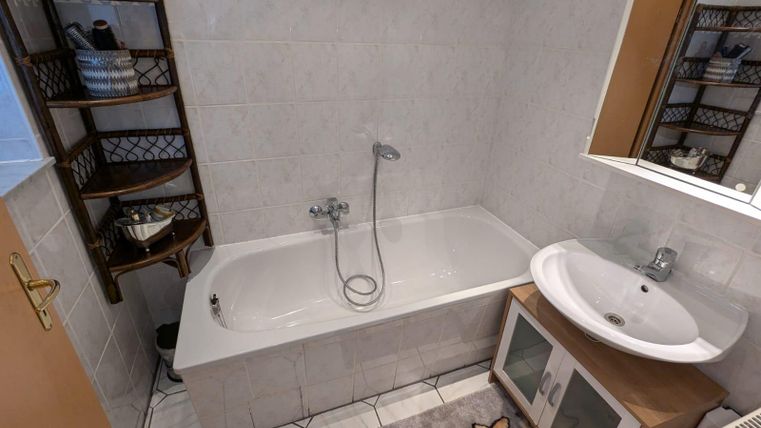 Ein Badezimmer mit einer Badewanne und einem Waschbecken. Regale an der Wand enthalten dekorative Elemente.
