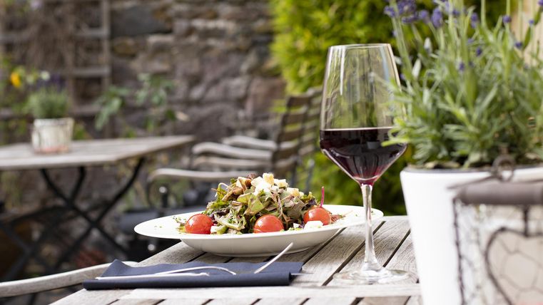 Ein Teller mit frischem Salat und Tomaten steht auf einem Holztisch. Neben dem Salat steht ein Glas Rotwein.