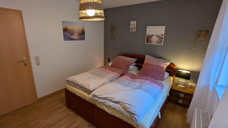 Ein gemütliches Schlafzimmer mit einem großen Doppelbett und sanften Farben. Eine warm leuchtende Lampe und dekorative Elemente sorgen für eine einladende Atmosphäre.
