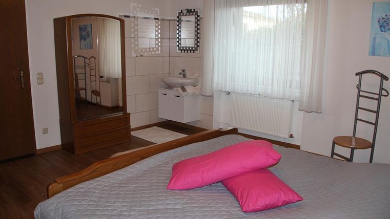 Ein gemütliches Schlafzimmer mit einem großen Bett und rosa Kissen. Der Raum hat ein Fenster und einen Schminkspiegel.