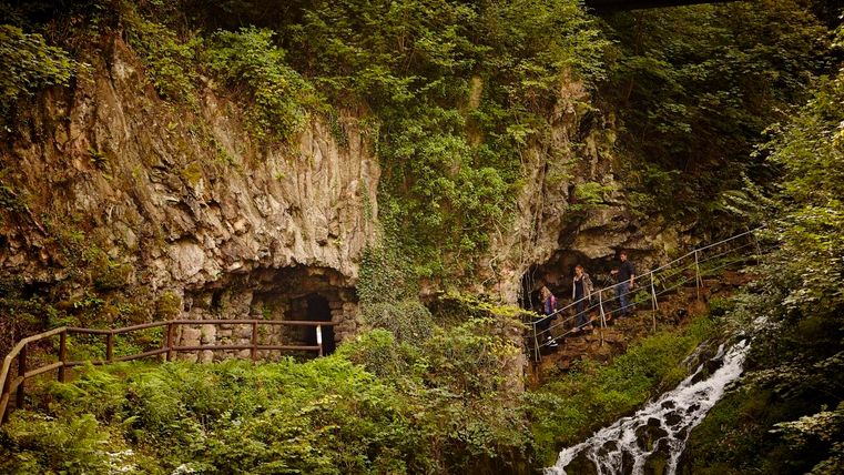 Eine beeindruckende Felsenlandschaft mit einem kleinen Wasserfall. Wanderer erkunden den schmalen Pfad entlang der Felsen.