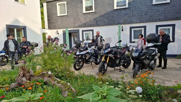 Eine Gruppe von Motorradfahrern steht vor mehreren Motorrädern in einem Garten.
