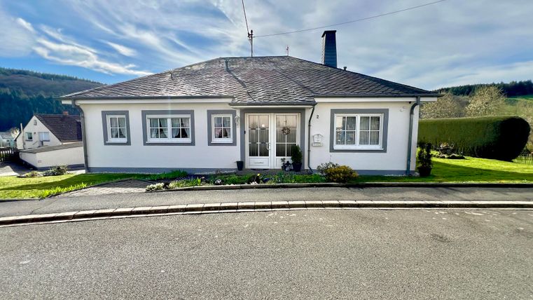 Ein modernes Einfamilienhaus mit einem flachen Dach. Es liegt in einer ruhigen Umgebung mit Grünflächen im Vordergrund.