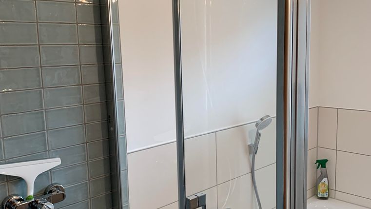 Ein modernes Badezimmer mit einer Dusche und einer Badewanne. Die Wände sind hell gefliest und es gibt verschiedene Pflegeprodukte auf dem Rand.