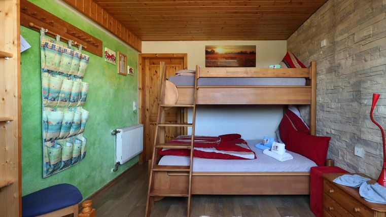Ein gemütliches Zimmer mit einem Hochbett und einem Einzelbett. Die Wände sind farbenfroh gestrichen und es gibt einfache Holzmöbel.