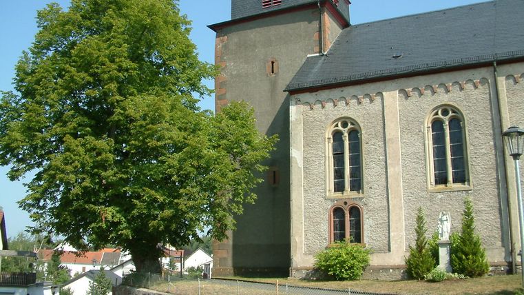 Pfarrkirche in Laufeld mit Baum und blauen Himmel.
