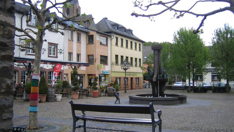 Ein schöner Platz mit einem Springbrunnen und Bäumen. Umgeben von bunten Gebäuden und Cafés.