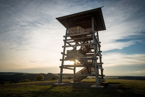 Houten uitkijktoren bij zonsondergang met weids uitzicht over het landschap.