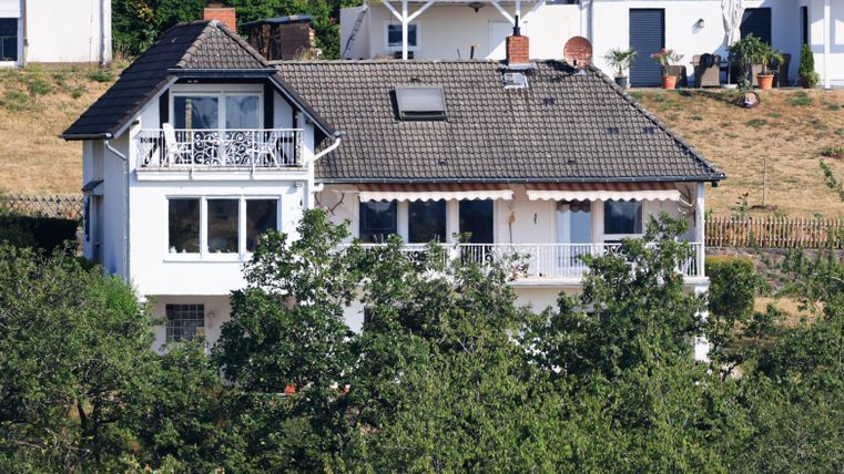 A modern house with a gable roof and a balcony. Surrounded by trees and green countryside.