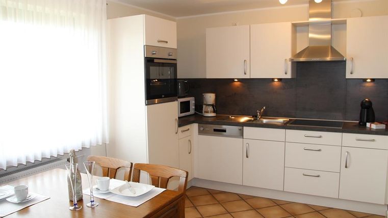 Eine moderne Küche mit weißen Schränken und einer dunklen Arbeitsplatte. Der Essbereich besteht aus einem Holztisch und Stühlen.