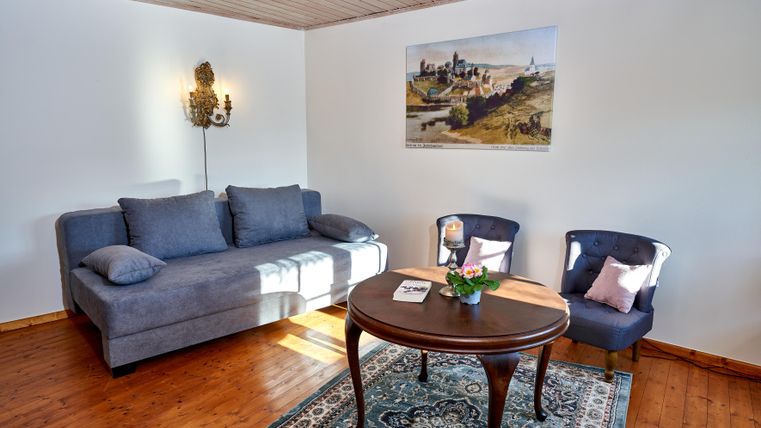 Ein elegant eingerichteter Wohnraum mit einem blauen Sofa und zwei Stühlen. Ein runder Tisch steht in der Mitte, während ein Bild an der Wand für eine dekorative Note sorgt.