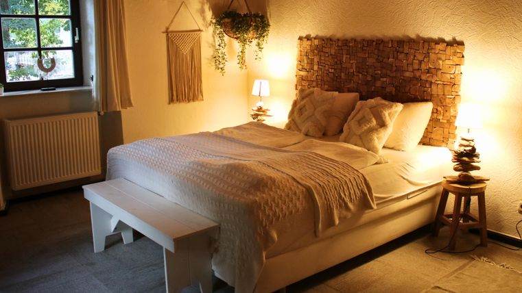 Ein gemütliches Schlafzimmer mit einem großen Bett und warmem Licht. Die Wände sind in sanften Farbtönen gehalten und es gibt dekorative Pflanzen.