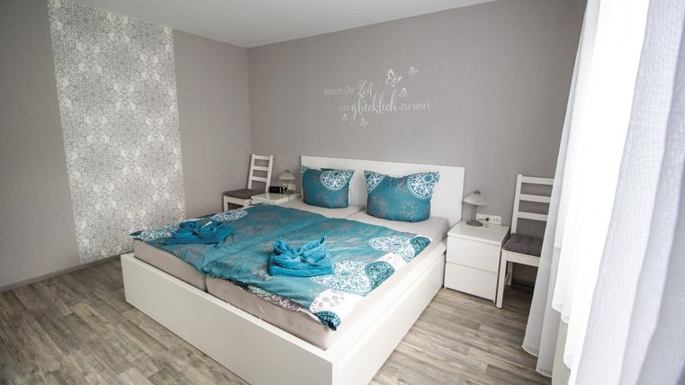 Ein modernes Schlafzimmer mit einem großen Bett und gemütlicher Bettwäsche in Blau. Die Wände sind neutral und es gibt zwei Stühle neben dem Bett.
