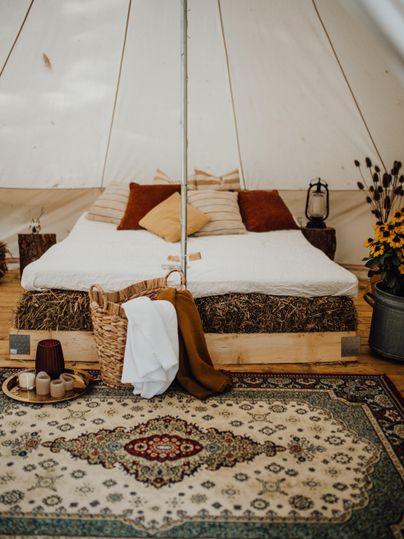 Ein gemütliches Zeltzimmer mit einem großen Bett, dekoriert mit bunten Kissen. Der Boden ist mit einem schönen Teppich bedeckt, und es gibt eine stilvolle Dekoration mit Blumen und Körben.