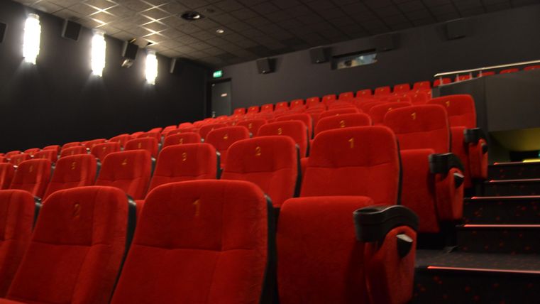 Ein leeres Kino mit roten Sitzen und gedämpfter Beleuchtung. Die Reihen sind ordentlich angeordnet und warten auf die Zuschauer.