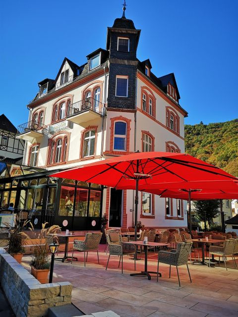 Ein elegantes Gebäude mit einem roten Sonnenschirm und Terrassenmöbeln. Der klare Himmel ergänzt die ansprechende Atmosphäre.