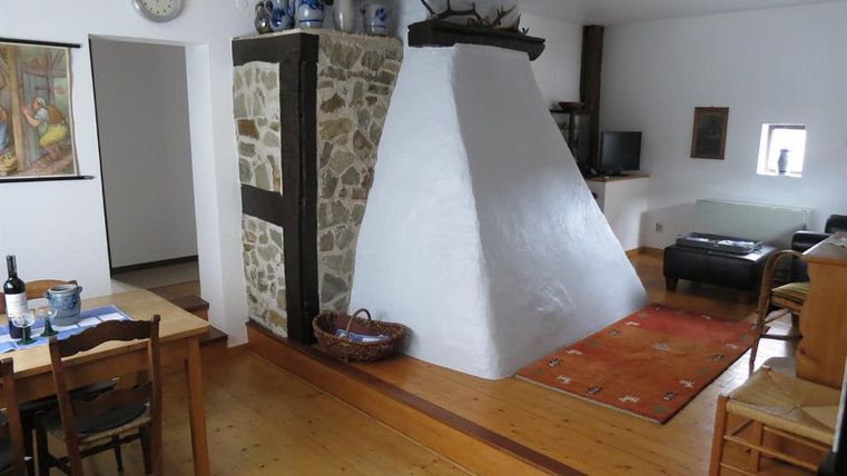 Ein gemütlicher Raum mit Holzboden und einer weißen Kaminecke. Es gibt einen Esstisch, Stühle und eine Couch in der Ecke.
