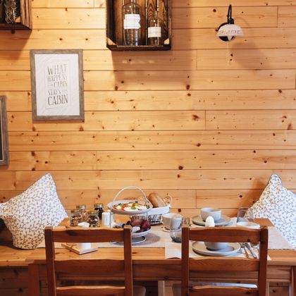 Ein gemütlicher Frühstückstisch in einem Holzmöbel. Der Tisch ist gedeckt mit Geschirr und leckerem Essen, umgeben von Kissen und warmen Holzton.