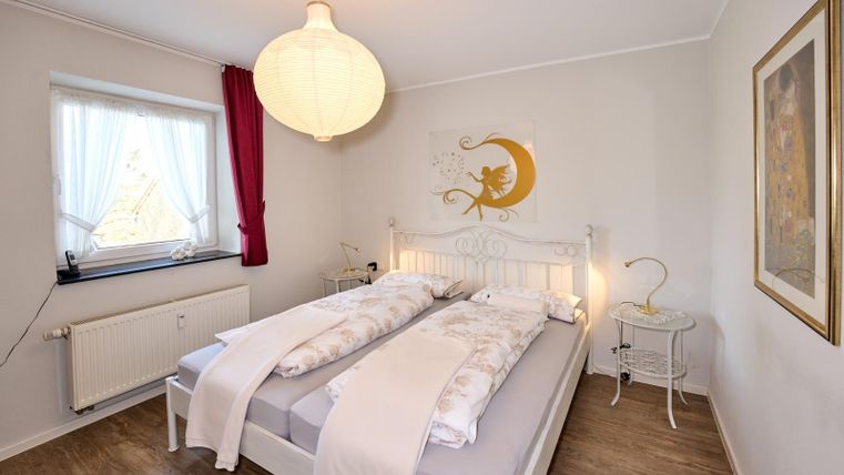 Ein helles Schlafzimmer mit einem Doppelbett und einer modernen Beleuchtung. Die Wände sind in sanften Farben gehalten und ein großes Fenster sorgt für viel Tageslicht.
