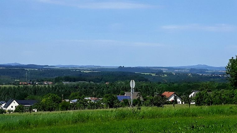 Eine weitläufige Landschaft mit sanften Hügeln und vereinzelten Häusern. Der Himmel ist klar und blau, ideal für einen entspannten Tag im Freien.