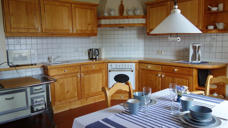 Eine gemütliche Küche mit Holzmöbeln und einer hellen Arbeitsfläche. Der Tisch ist für eine Mahlzeit gedeckt und die Atmosphäre ist einladend.