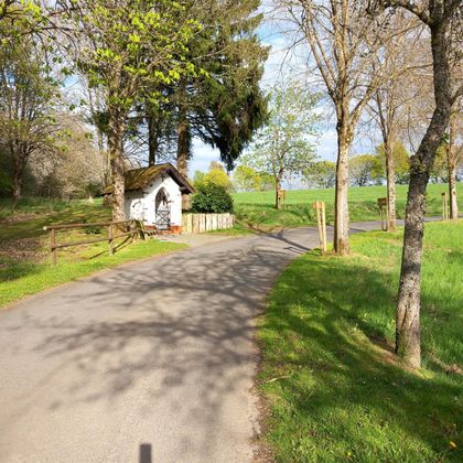 A picturesque path that leads through a green landscape. By the path stands a small, traditional hut, surrounded by trees.