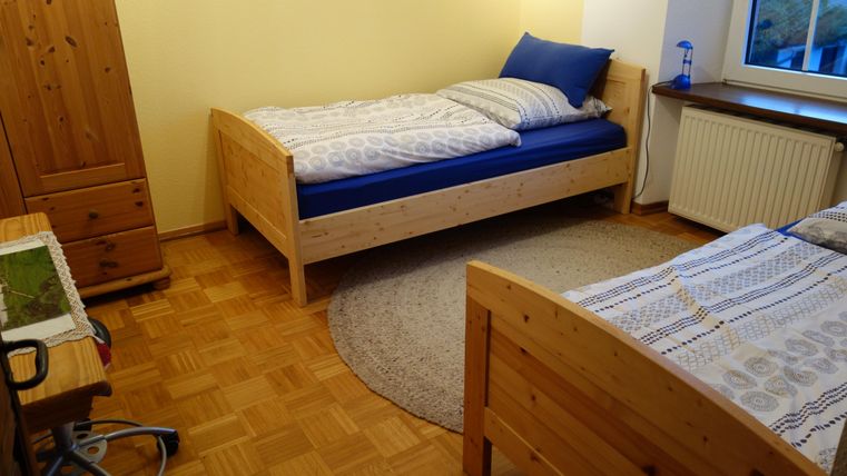 Ein einfaches Schlafzimmer mit zwei Betten und einem runden Teppich. Die Wände sind gelb gestrichen, und das Zimmer wirkt hell und einladend.
