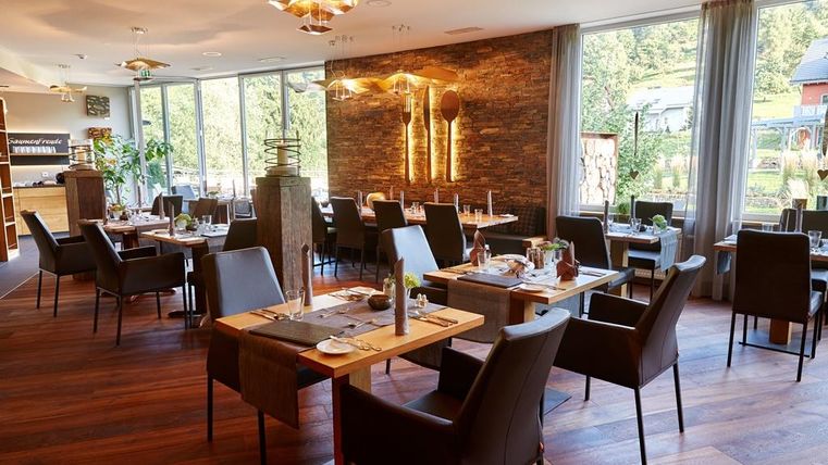 Ein elegantes Restaurant mit modernen Tischen und Stühlen. Große Fenster bieten einen Blick auf die Natur.