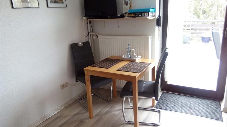 Ein kleiner Essbereich mit einem Holztisch und zwei Stühlen. An der Wand hängen Bilder und ein Fernseher steht auf einem Regal.
