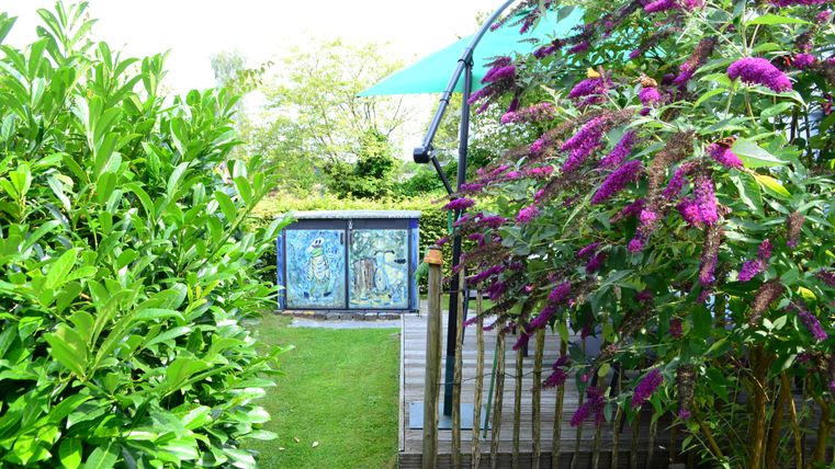 Ein freundlicher Garten mit üppigem Grün und bunten Blumen. Im Hintergrund sind dekorative Kunstwerke sichtbar.