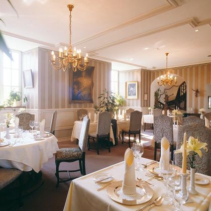 Ein elegantes Restaurant mit schön eingedeckten Tischen und stilvollen Stühlen. Die warmen Farben und die dekorativen Elemente schaffen eine einladende Atmosphäre.