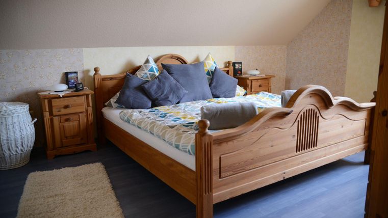 Ein gemütliches Schlafzimmer mit einem großen Holzbett und bunten Kissen. Neben dem Bett stehen zwei Nachttische und ein Korb.