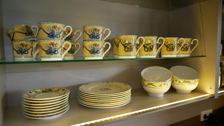 Ein Regal mit buntem Geschirr. Oben stehen Tassen mit floralen Mustern und unten Teller sowie Schalen.