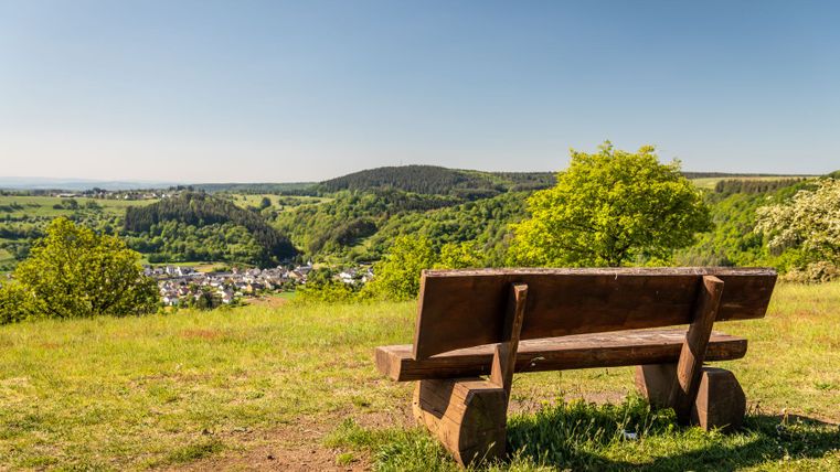 Holzbank mit Blick auf grüne Landschaft und Dorf in der Ferne.
