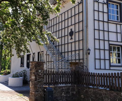 Ein charmantes Gebäude mit einer hellen Fassade und einem schönen Treppenaufgang. Im Vordergrund befinden sich eine Steinmauer und ein gepflegter Garten.