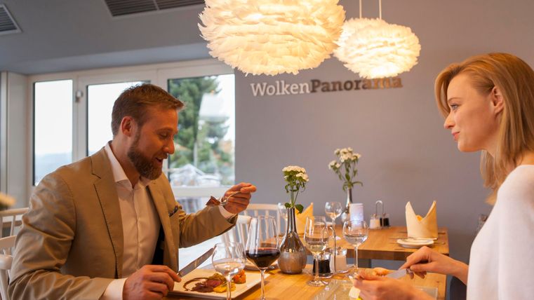 Ein elegantes Restaurant mit einem Paar, das gemeinsam Essen genießt. Die Atmosphäre ist warm und einladend, mit modernen Lampen und Blick nach draußen.