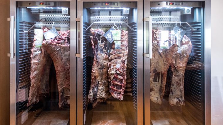 Drei Kühlschränke mit ausgereiftem Fleisch sind nebeneinander angeordnet. Das Fleisch ist sichtbar aufgehängt und weist unterschiedliche Sorten auf.
