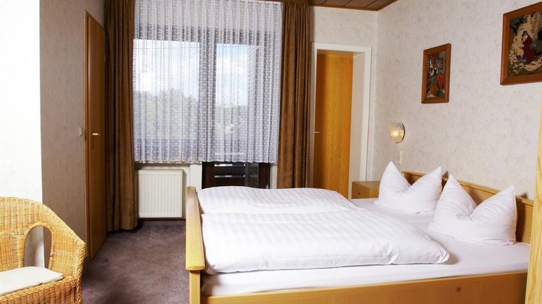 Ein einfaches Schlafzimmer mit einem Doppelbett und zwei Kissen. Ein gemütlicher Sessel und große Fenster sorgen für viel Licht.