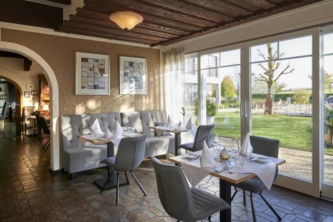 Ein einladendes Restaurant mit eleganten Tischen und Stühlen. Große Fenster bieten einen Blick auf den Außenbereich mit Grünflächen.