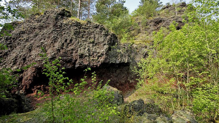 Eine felsige Landschaft mit grünen Pflanzen und Bäumen. Das Gelände hat eine unebene Struktur und zeigt vulkanische Gesteine.
