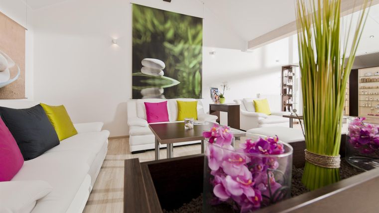 Ein modernes Wohnzimmer mit weißen Sofas und bunten Kissen. Im Hintergrund befindet sich ein großes Bild von grünen Pflanzen und eine elegante Blumenarrangierung auf dem Tisch.